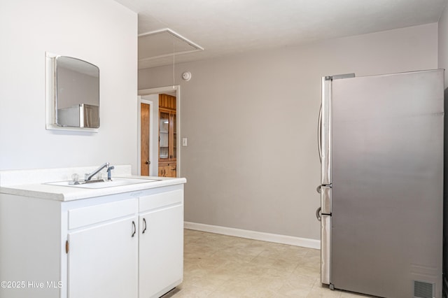 kitchen with white cabinets, light countertops, baseboards, a sink, and freestanding refrigerator