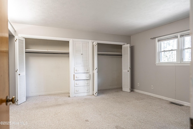 unfurnished bedroom featuring baseboards, multiple closets, visible vents, and carpet flooring