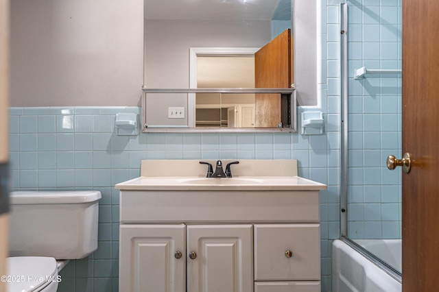 bathroom featuring tile walls, toilet, vanity, enclosed tub / shower combo, and wainscoting