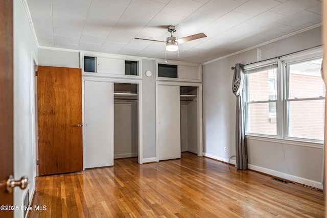 unfurnished bedroom featuring visible vents, multiple closets, ornamental molding, and light wood-style floors