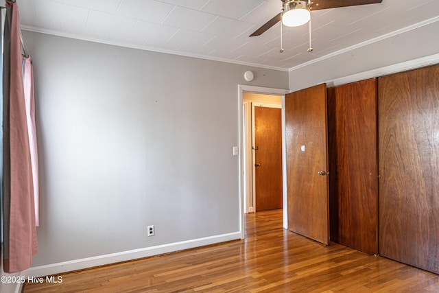 unfurnished bedroom featuring a closet, crown molding, baseboards, and wood finished floors