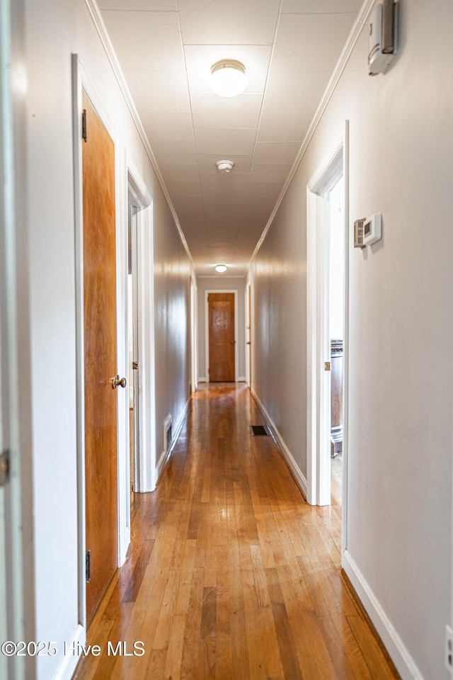 corridor featuring ornamental molding, baseboards, and light wood-type flooring