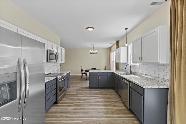 kitchen with light wood-type flooring, a chandelier, white cabinetry, stainless steel appliances, and a sink