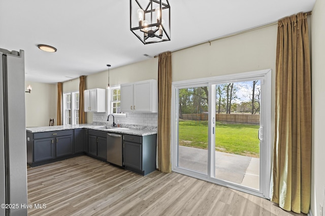 kitchen with light wood-style flooring, gray cabinets, a chandelier, a sink, and backsplash
