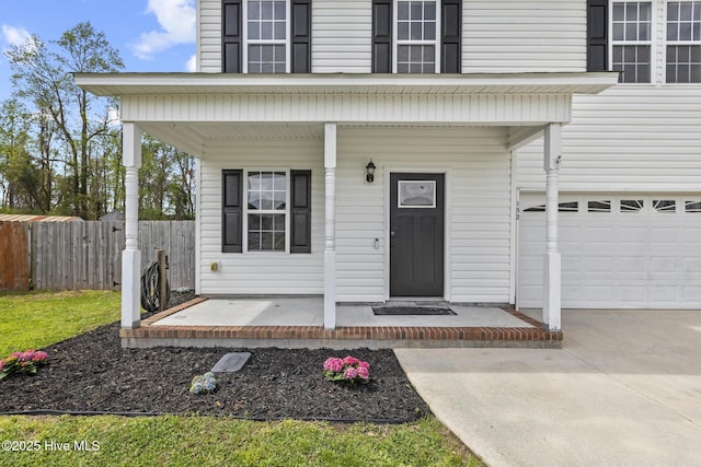 view of exterior entry featuring concrete driveway, a porch, fence, and an attached garage