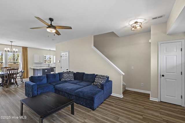 living room featuring visible vents, baseboards, dark wood-style flooring, stairway, and ceiling fan with notable chandelier