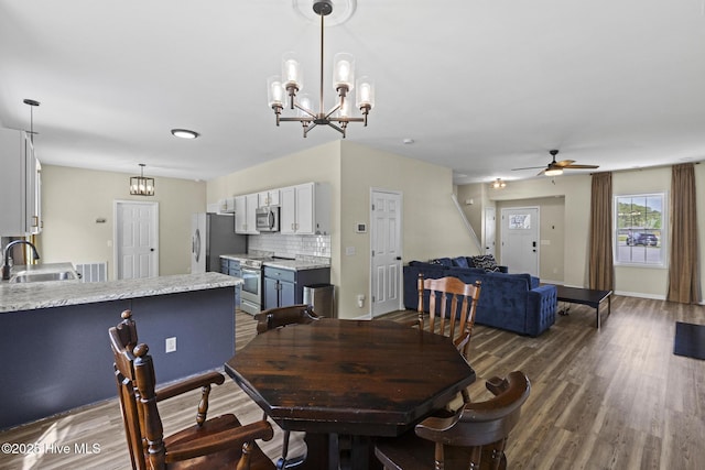 dining room with dark wood-type flooring, ceiling fan with notable chandelier, and baseboards