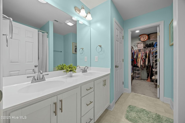 bathroom featuring a sink, visible vents, double vanity, and a walk in closet