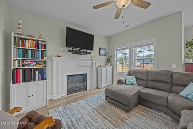 living area featuring a glass covered fireplace, light wood finished floors, visible vents, and a ceiling fan