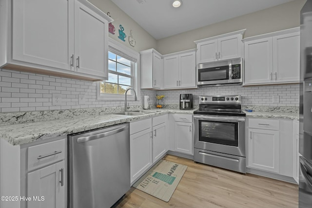 kitchen with a sink, white cabinetry, stainless steel appliances, backsplash, and light wood-style flooring