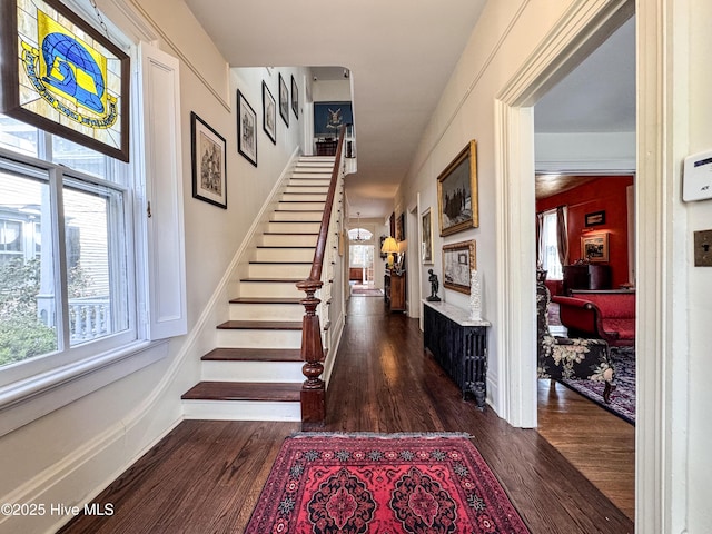foyer featuring a fireplace, dark wood-style floors, a wealth of natural light, and stairway