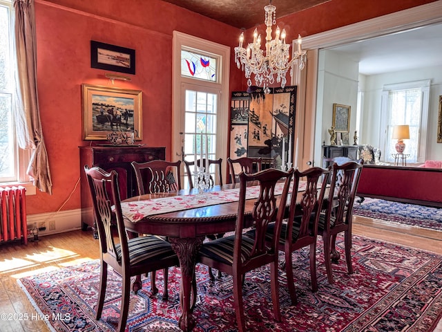 dining room featuring wood-type flooring, radiator heating unit, plenty of natural light, and an inviting chandelier