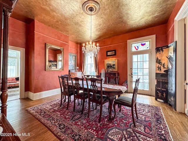 dining area with light wood-type flooring, baseboards, a textured ceiling, and a chandelier
