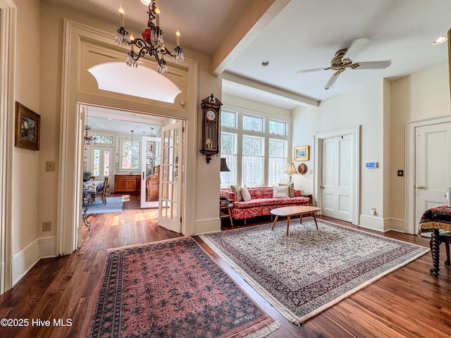 foyer entrance featuring baseboards, a healthy amount of sunlight, dark wood-style floors, and ceiling fan with notable chandelier