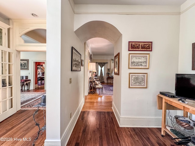 hallway featuring arched walkways, baseboards, and dark wood-style flooring