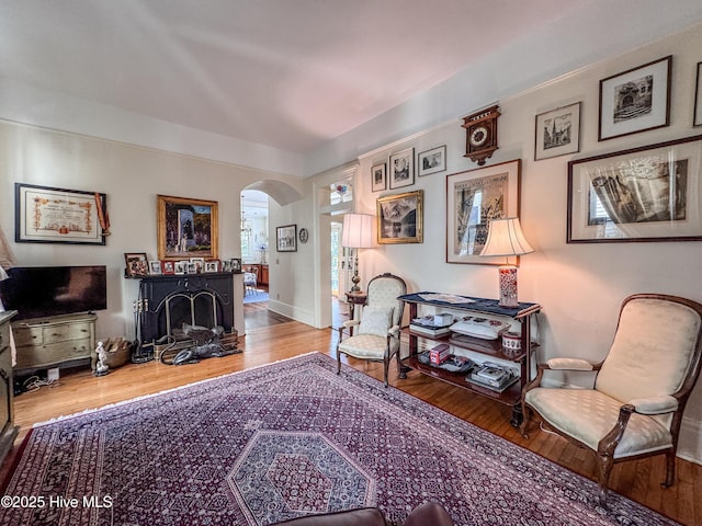 living area featuring arched walkways, wood finished floors, a fireplace, and baseboards