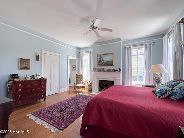 bedroom with a ceiling fan, a brick fireplace, and wood finished floors