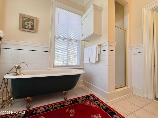 bathroom featuring tile patterned floors, tile walls, wainscoting, a soaking tub, and a stall shower