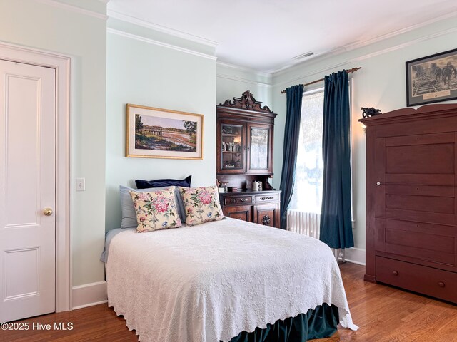 bedroom featuring wood finished floors, visible vents, and ornamental molding