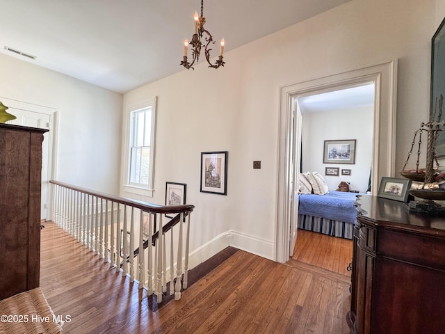 corridor featuring hardwood / wood-style floors, visible vents, an upstairs landing, baseboards, and a notable chandelier