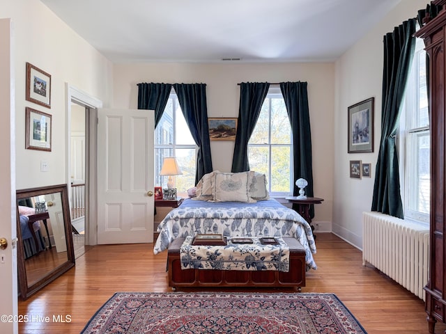 bedroom featuring radiator heating unit, multiple windows, light wood finished floors, and visible vents