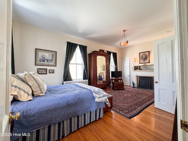 bedroom with radiator heating unit, wood finished floors, and a fireplace