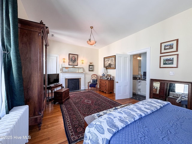 bedroom featuring a fireplace, radiator, wood finished floors, and visible vents