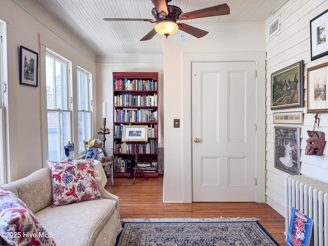 living area with radiator, wood finished floors, and crown molding