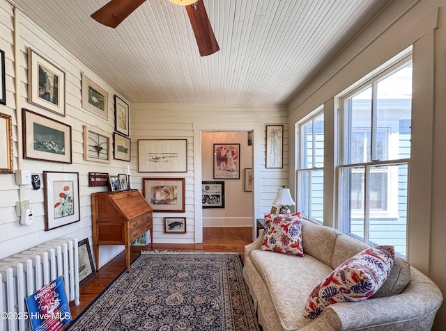 sitting room featuring radiator heating unit, wooden walls, wood finished floors, wooden ceiling, and ceiling fan