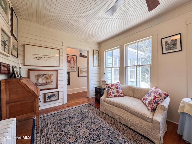 living room with baseboards, wooden walls, wood finished floors, and ceiling fan