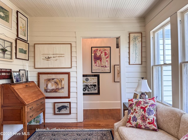 sitting room featuring baseboards, wooden walls, wood finished floors, and a wealth of natural light