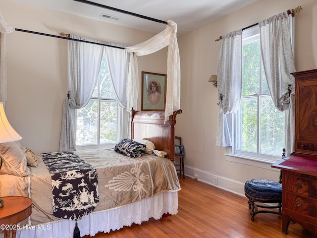 bedroom featuring baseboards, wood finished floors, multiple windows, and visible vents