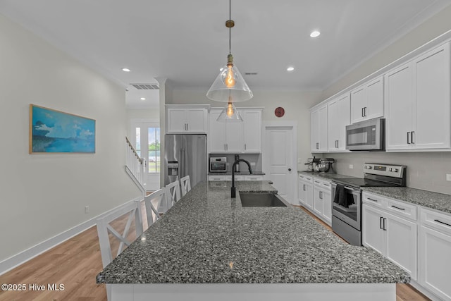 kitchen featuring visible vents, a sink, stainless steel appliances, white cabinetry, and an island with sink