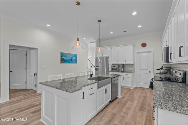 kitchen with appliances with stainless steel finishes, a center island with sink, light wood-type flooring, a sink, and white cabinetry