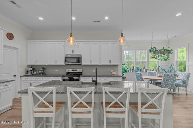 kitchen with white cabinets, a sink, light wood finished floors, dark stone countertops, and stainless steel appliances