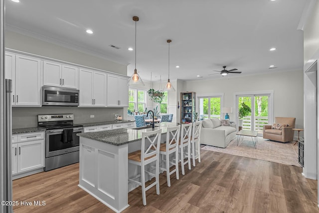 kitchen with white cabinets, appliances with stainless steel finishes, a ceiling fan, open floor plan, and visible vents