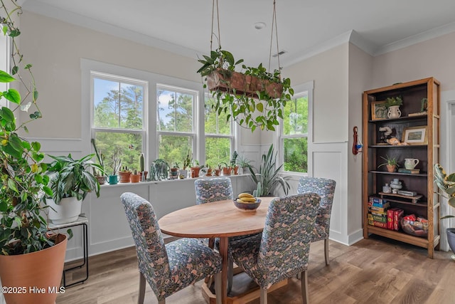 dining space featuring crown molding, light wood-style floors, a decorative wall, and wainscoting