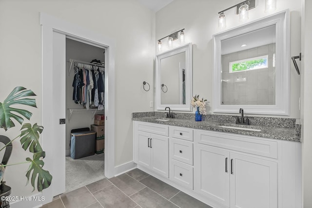 bathroom featuring double vanity, a walk in closet, a sink, and tile patterned flooring
