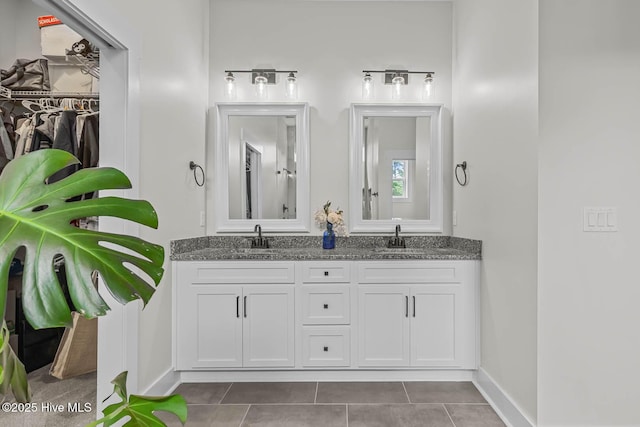 full bathroom with double vanity, baseboards, a walk in closet, tile patterned floors, and a sink
