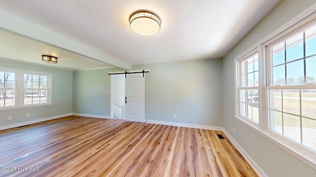empty room with beam ceiling, visible vents, a barn door, baseboards, and light wood-style floors