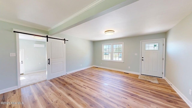 foyer entrance with light wood finished floors, crown molding, a barn door, and baseboards