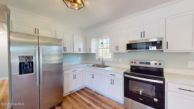 kitchen featuring white cabinets, appliances with stainless steel finishes, ornamental molding, and a sink