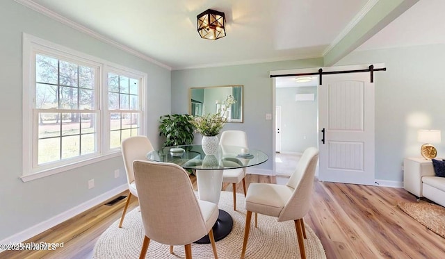 dining area with light wood-style flooring, a barn door, baseboards, and a healthy amount of sunlight