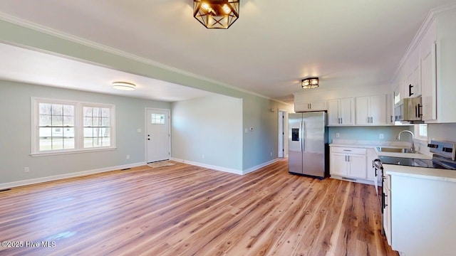 kitchen featuring stainless steel fridge, light wood-style flooring, a sink, white cabinets, and baseboards