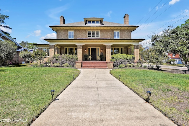 american foursquare style home with a chimney, covered porch, a front yard, and brick siding