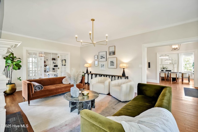 living area featuring wood finished floors, a notable chandelier, ornamental molding, and baseboards