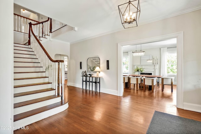foyer featuring crown molding, a fireplace, wood finished floors, stairs, and baseboards