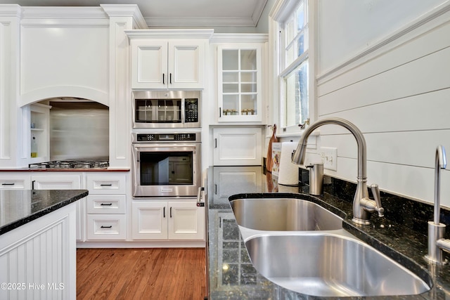 kitchen with glass insert cabinets, white cabinets, a sink, dark stone counters, and stainless steel appliances