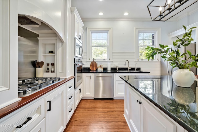 kitchen featuring white cabinets, a sink, light wood-style floors, crown molding, and stainless steel appliances