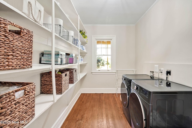 clothes washing area with laundry area, crown molding, wood finished floors, baseboards, and washer and clothes dryer